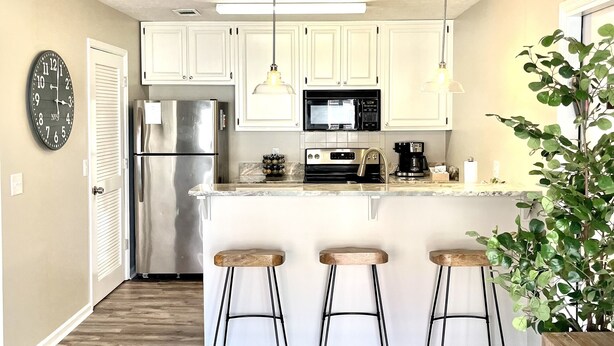 A modern kitchen with white cabinets, a stainless steel refrigerator, a microwave, and a bar area with stools. - LOCATION! | Walk to Stadium and Toomer’s | Cozy 4BR Condo in the Heart of Auburn (Auburn)