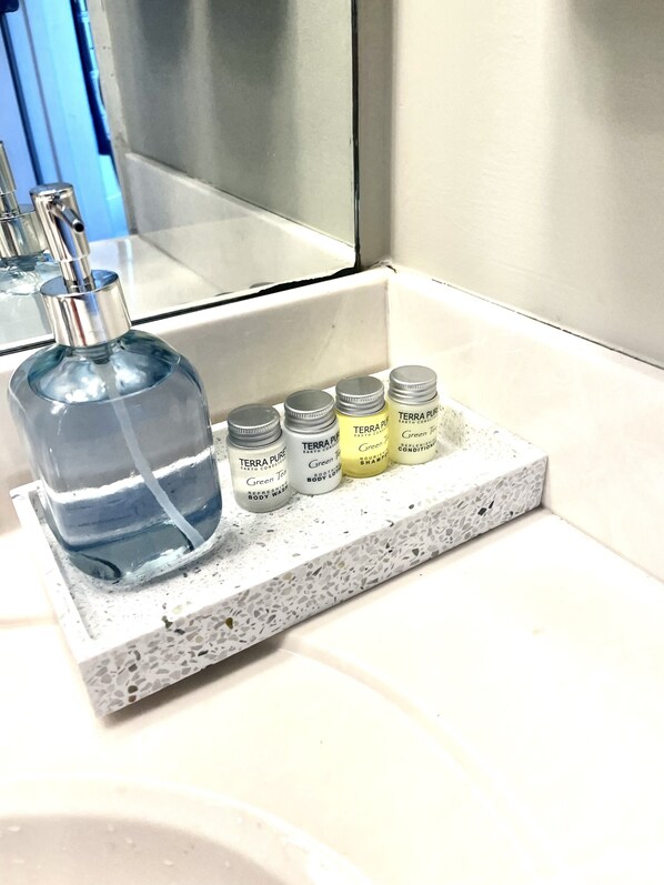 Un estante de baño con una botella grande de agua y cuatro botellas más pequeñas de crema hidratante y acondicionador Terra Pure.