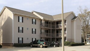 A multi-story building with a central atrium, balconies, and a parking area with vehicles. - LOCATION! | Walk to Stadium and Toomer’s | Cozy 4BR Condo in the Heart of Auburn (Auburn)