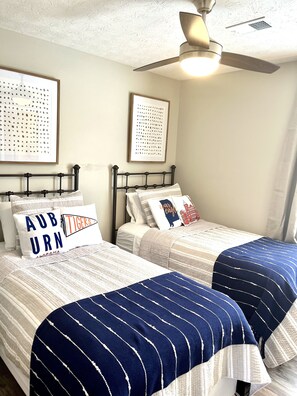 A bedroom with two beds, each with a striped bedspread, a ceiling fan, and framed artwork on the walls.