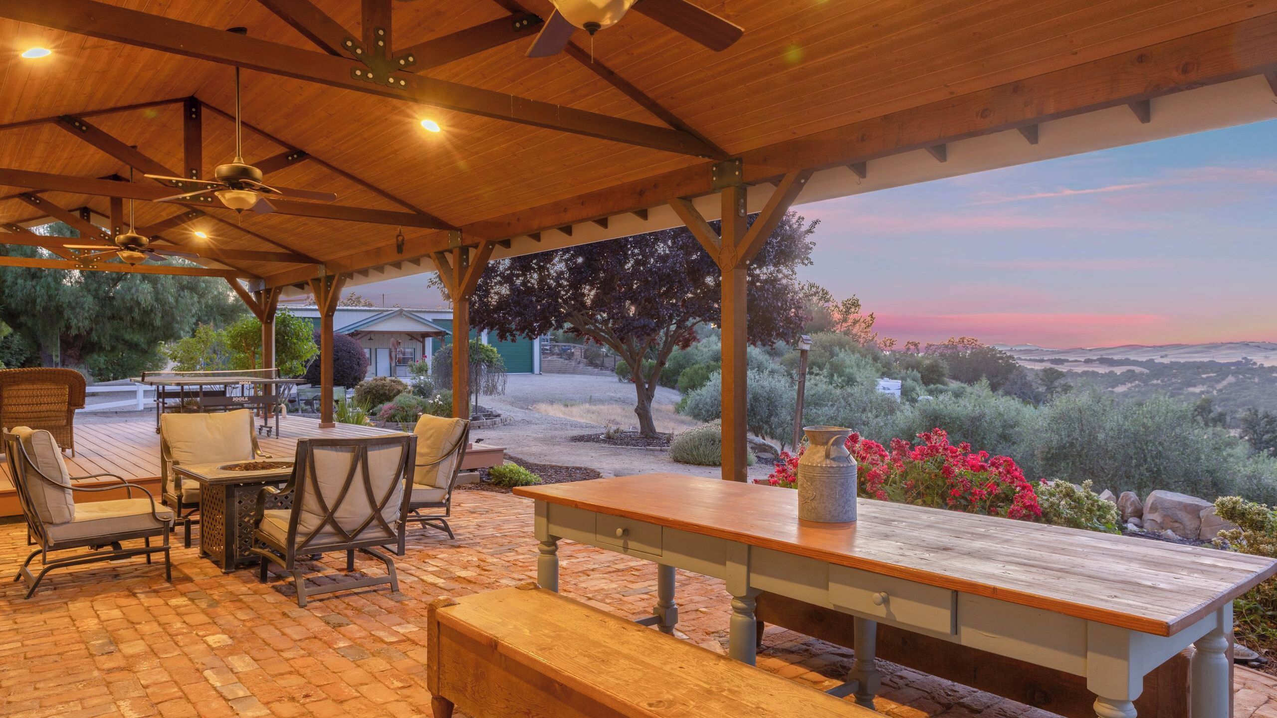 Un patio cubierto con mobiliario exterior, una mesa de madera y vistas del paisaje.