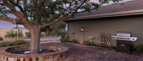 A backyard with a brick fire pit, a tree, and a grill.