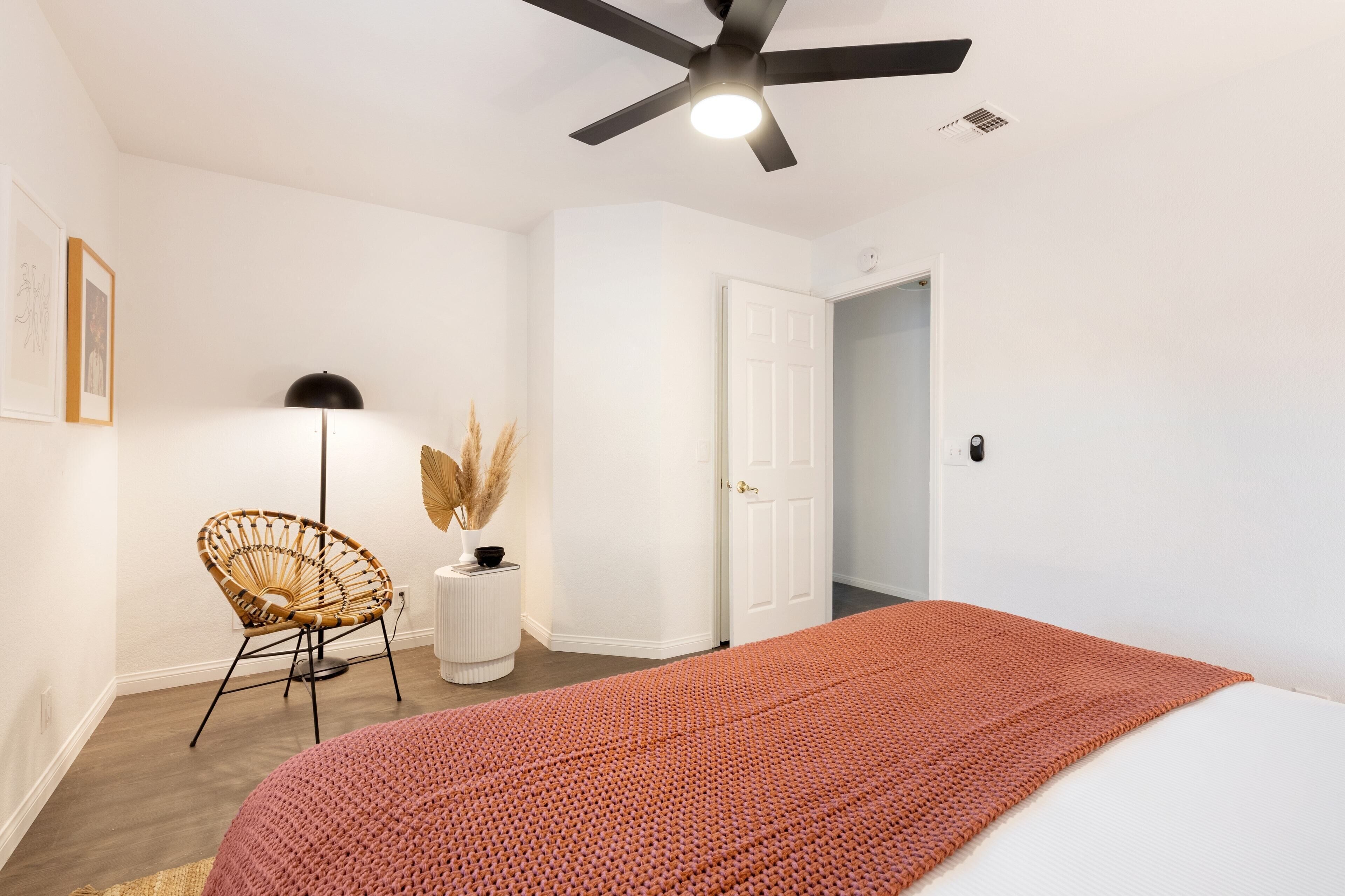 Un dormitorio con cama, ventilador de techo, puerta, silla y lámpara.