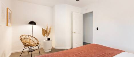 Un dormitorio con cama, ventilador de techo, puerta, silla y lámpara.