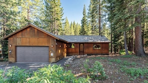 A wooden cabin with a garage, surrounded by a forest.