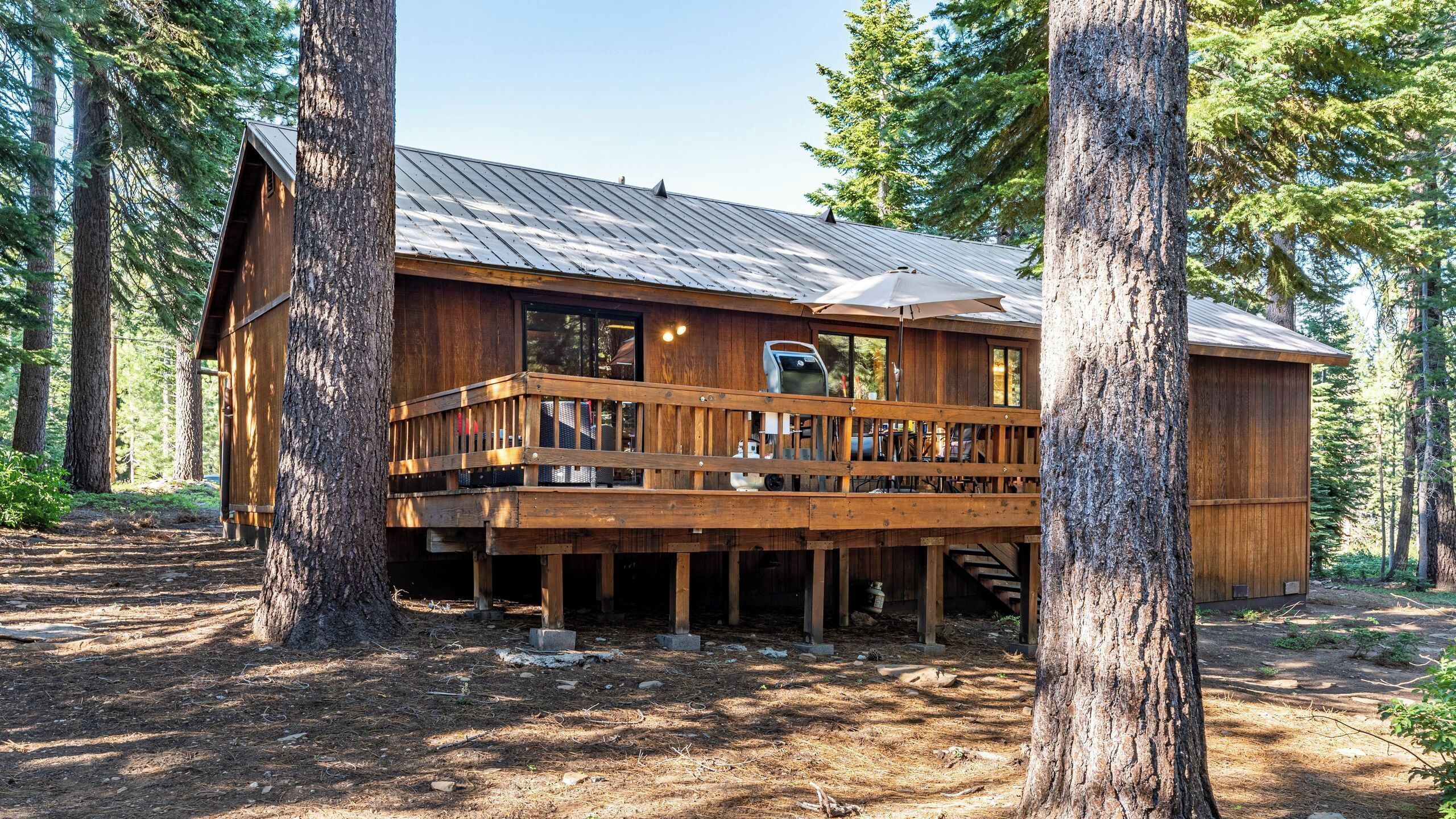 A wooden cabin with a deck, surrounded by trees.