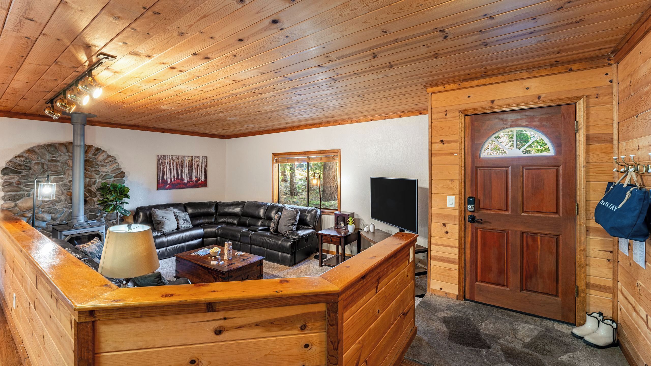 A log cabin interior with a stone fireplace, a leather sofa, a wooden bench, and a wooden door with a window.