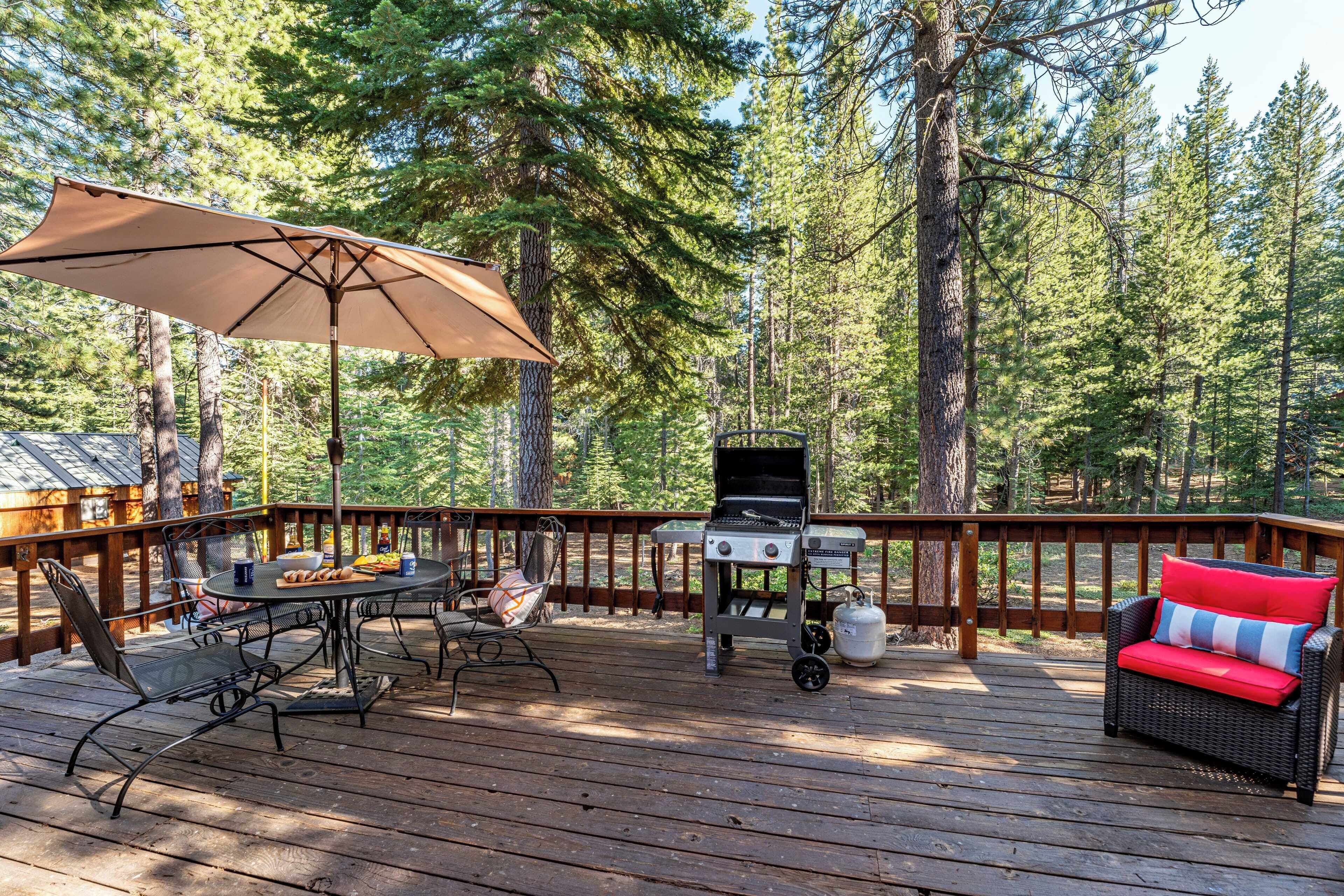 A wooden deck with a grill, a table with chairs, and a wicker sofa with a red cushion.