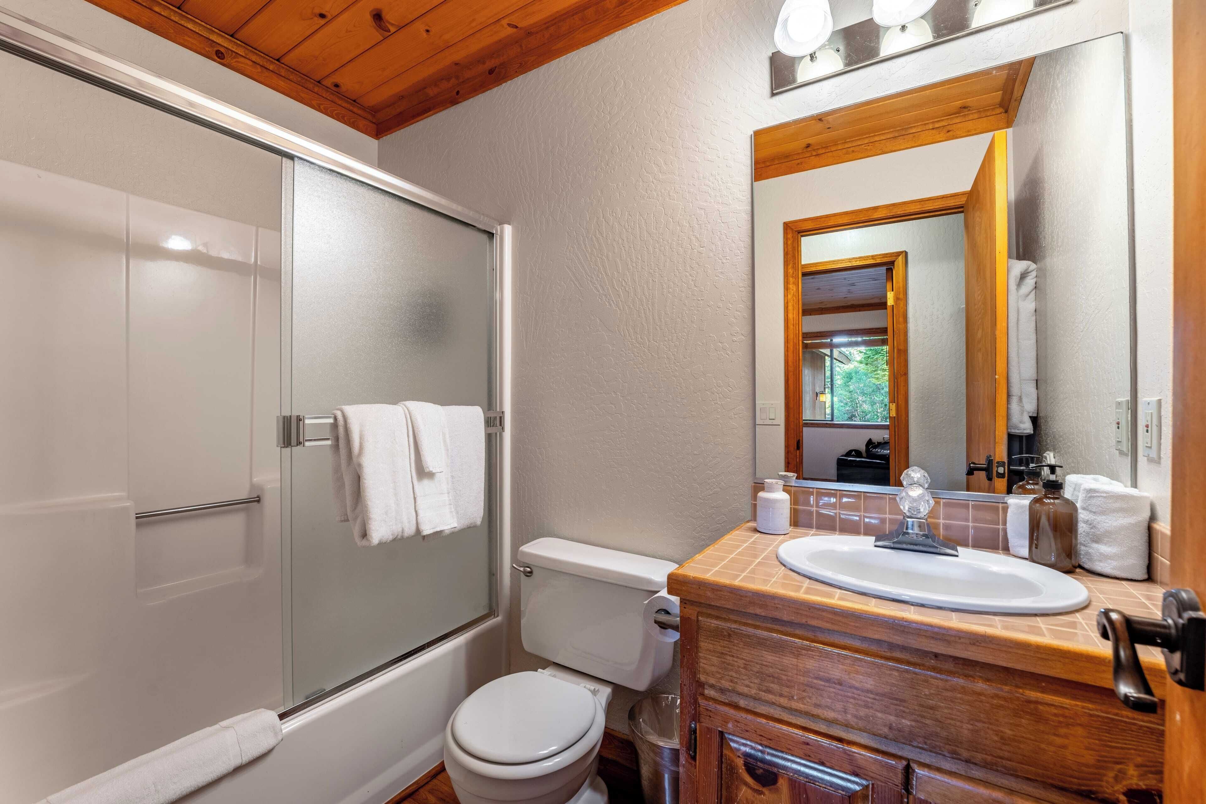 Een badkamer met een glazen douchecabine, toilet, houten wastafelmeubel met een wastafel en een grote spiegel.