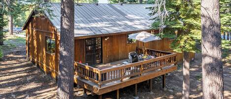 A wooden cabin with a deck, surrounded by trees.