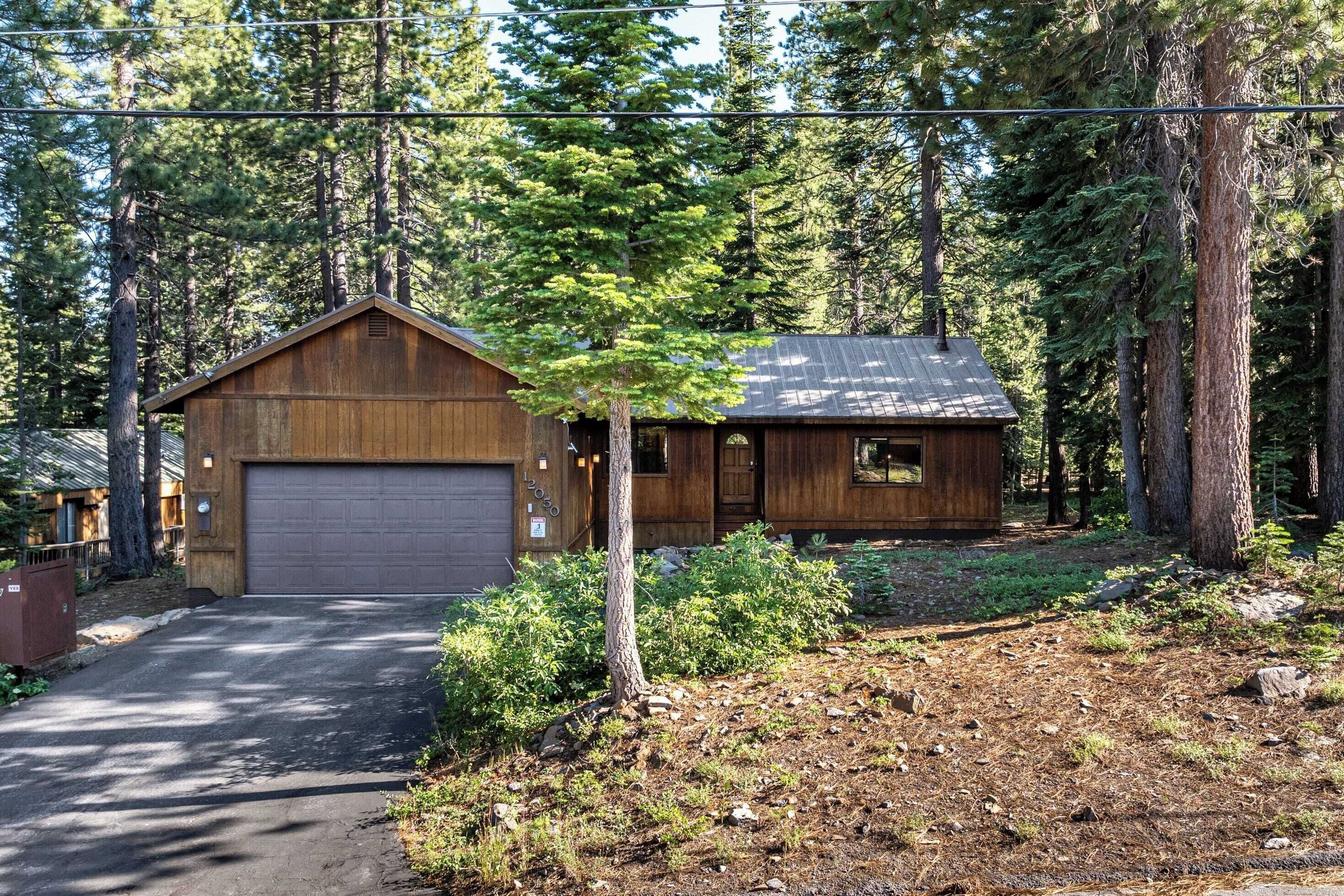 A two-story wooden cabin with a garage, surrounded by dense forest.