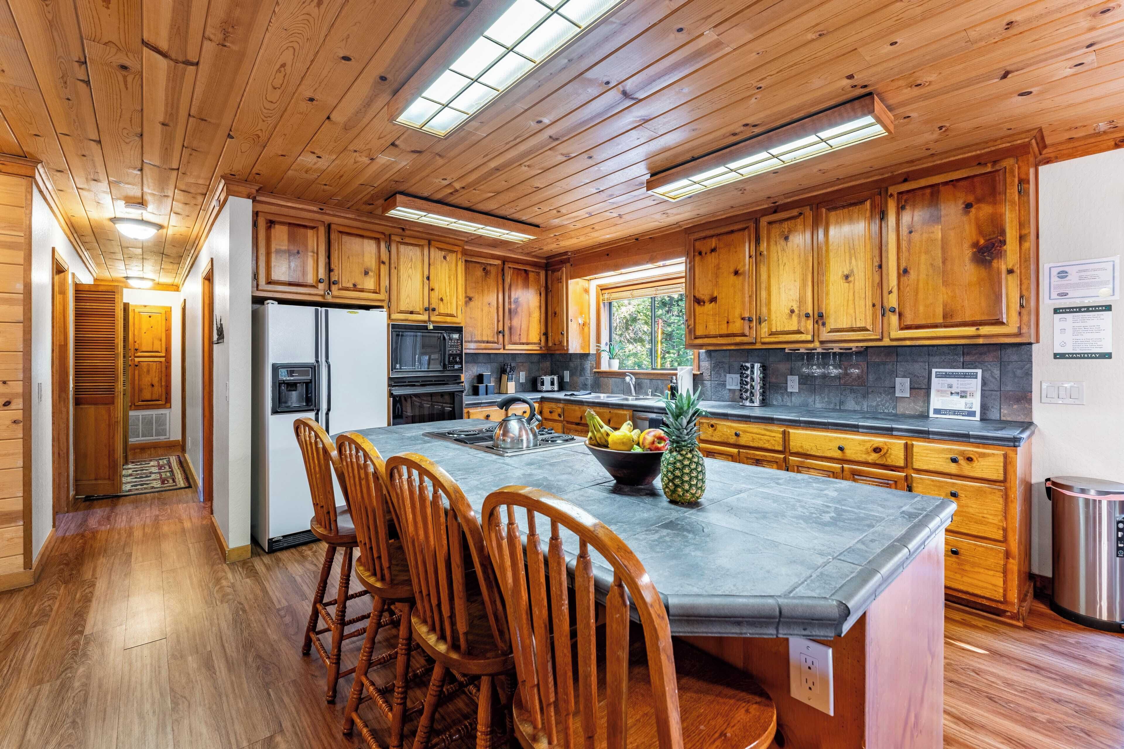 A kitchen with wooden cabinets, a granite countertop, and a central island with chairs.