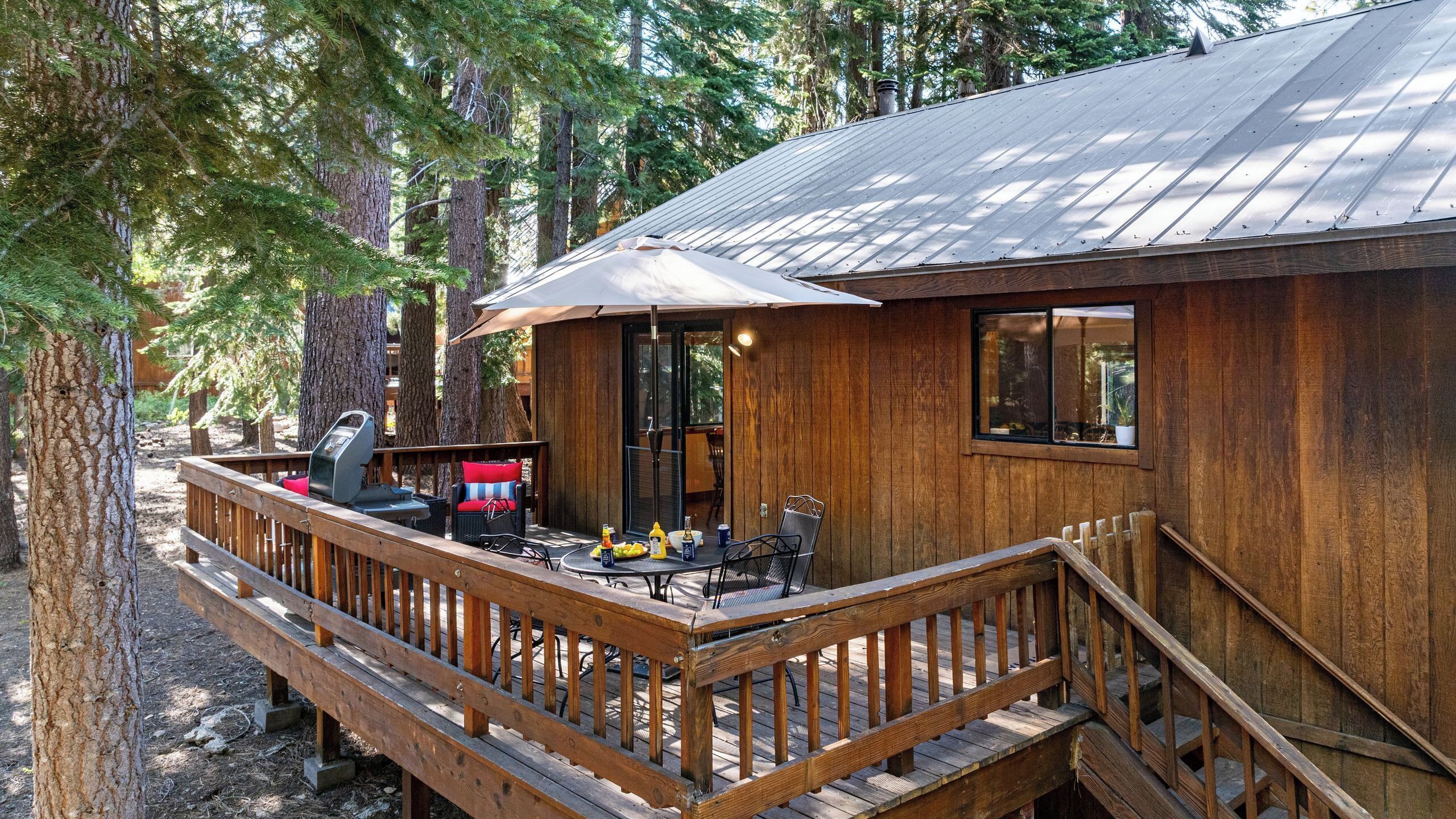A wooden cabin with a deck, outdoor seating, and a grill.