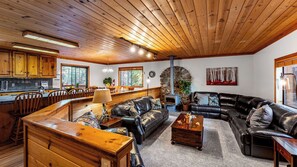 A cozy cabin interior with a wooden ceiling, a stone fireplace, a dining area, and a living room with leather sofas. - Whiskey Springs by Avantstay Classic Cabin Near Tahoe Donner Ski Area! (Truckee)