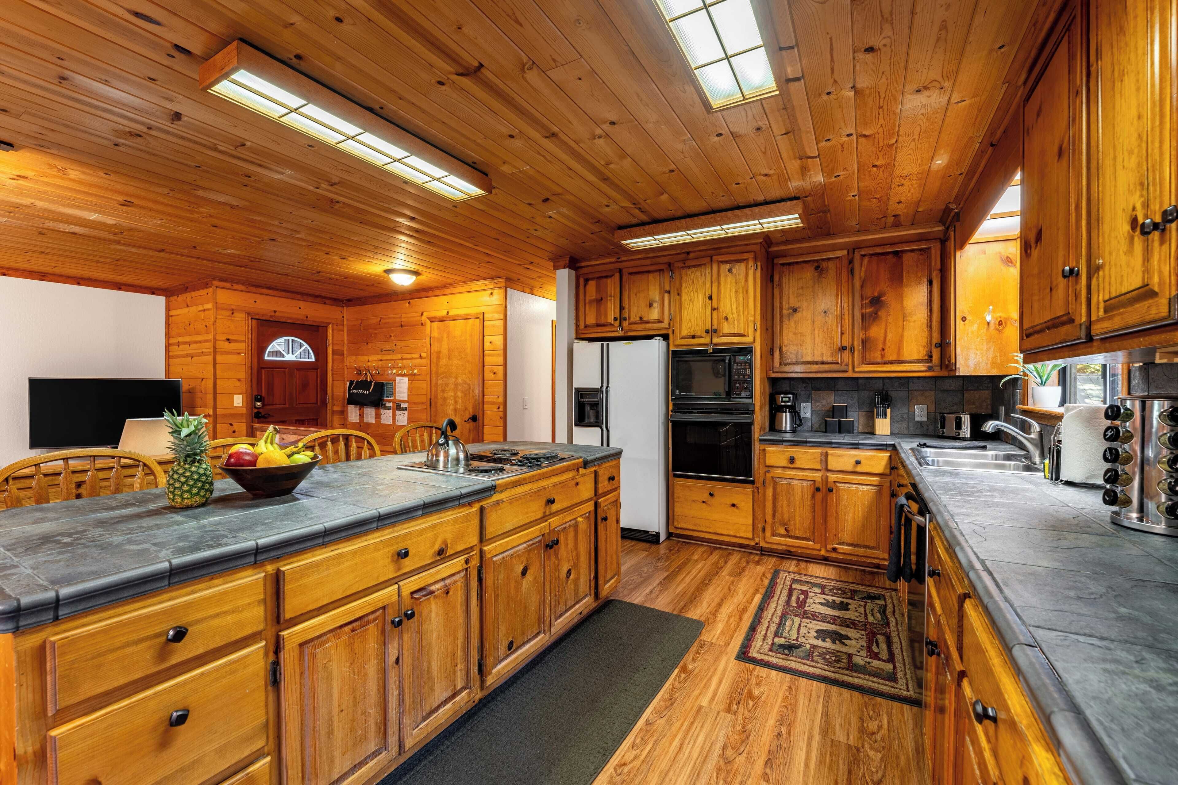 A wooden cabin-style kitchen with a large island, wooden cabinets, and a stone countertop.