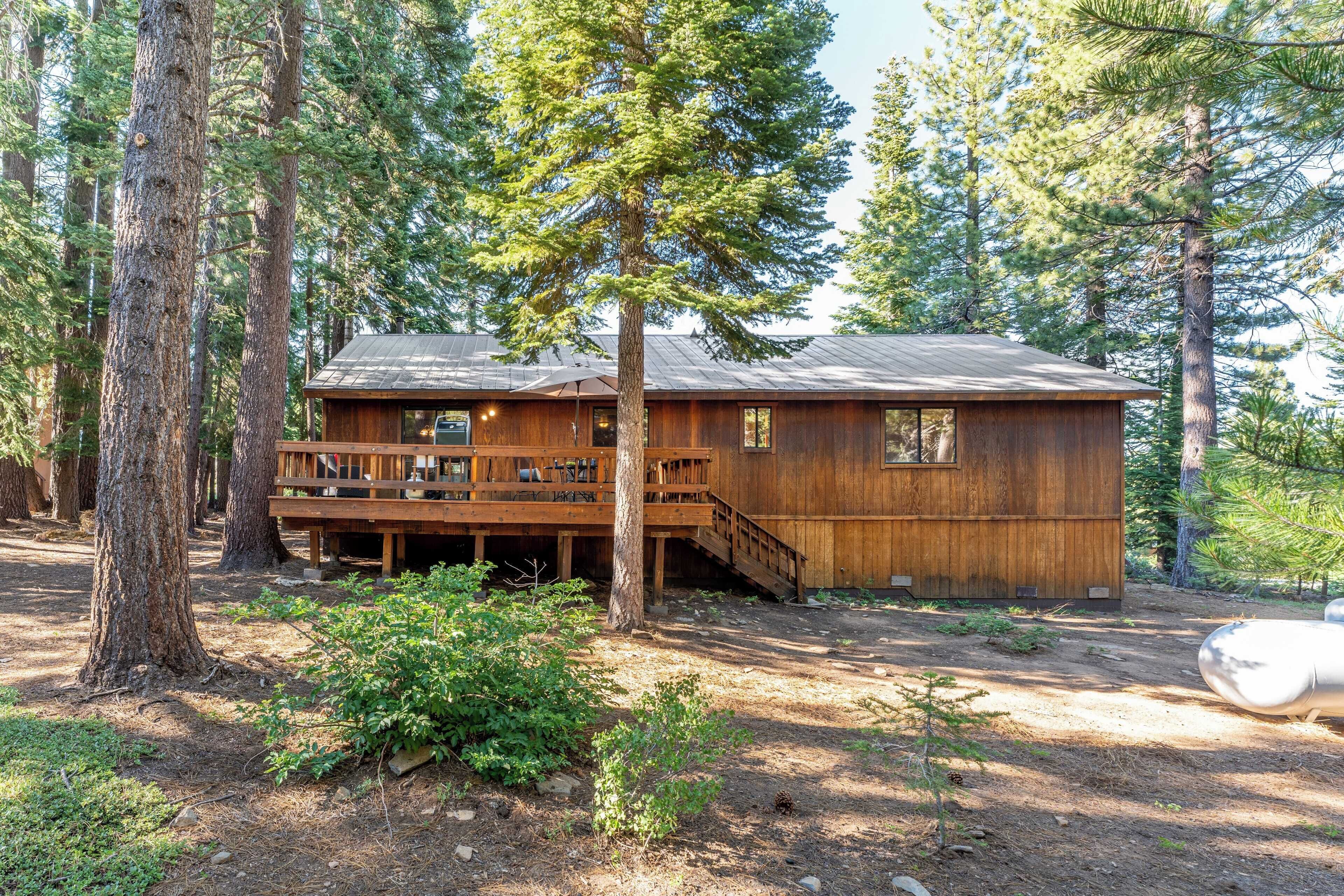 A wooden cabin with a deck, surrounded by tall trees.