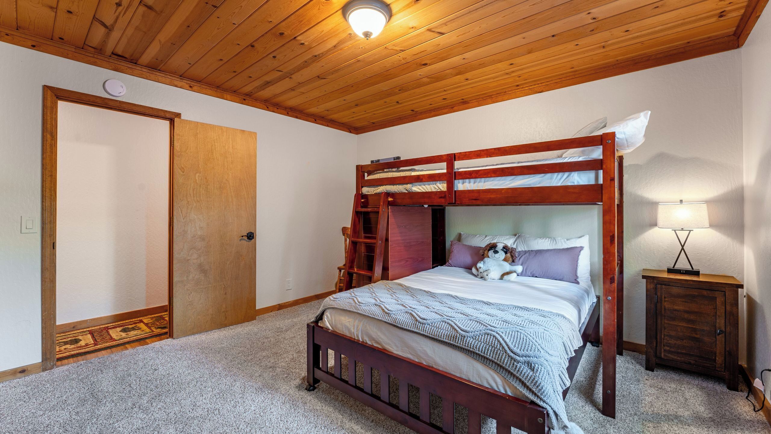 A bunk bed with a ladder, a bedside lamp, and a plush toy on the bed.