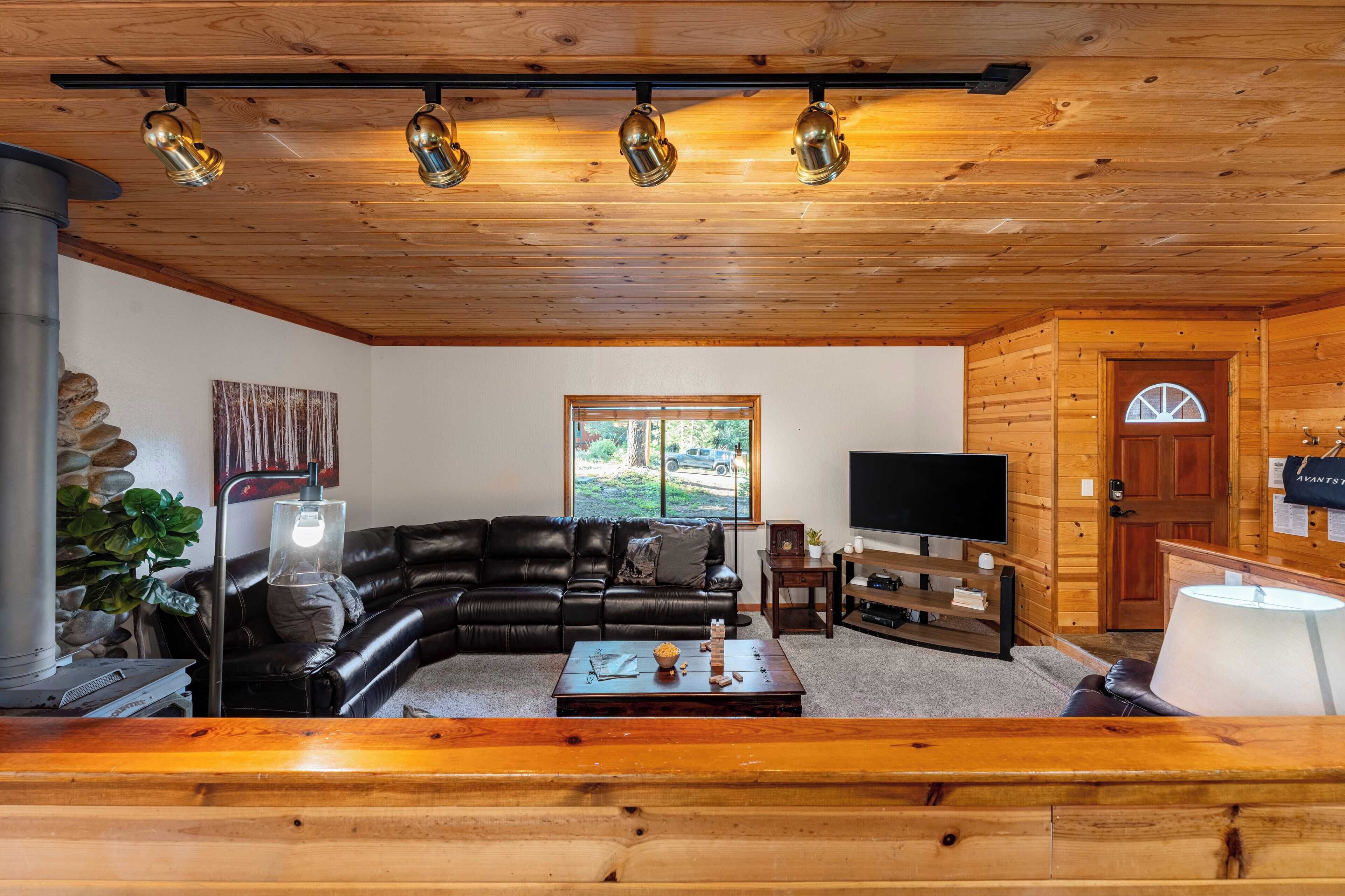 Ein gemütliches Wohnzimmer mit Holzbalkendecke, einer schwarzen Ledersofa, einem Fernseher und einer Wanddekoration aus Stein.