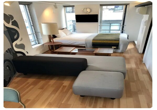 Une pièce de taille modeste comprenant un lit, un canapé, un pouf et une petite table.