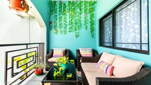 Un balcón con dos sofás de mimbre, una mesita pequeña y plantas colgantes frente a una pared color turquesa.