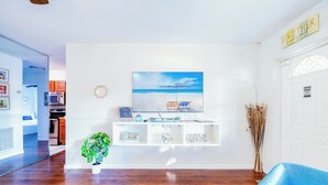 Un salon doté d’un plancher en bois, d’un fauteuil bleu, d’une console blanche agrémentée d’objets décoratifs et d’un tableau sur le thème de la plage.