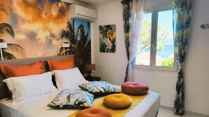 A bed with multiple pillows, a wall mural, a window with curtains, and a lamp. - GOLDEN VILLA (HYERES)