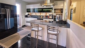 A modern kitchen with a central island, stainless steel appliances, and bar stools. - GOLDEN VILLA (HYERES)