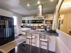 A modern kitchen with a central island, stainless steel appliances, and bar stools.