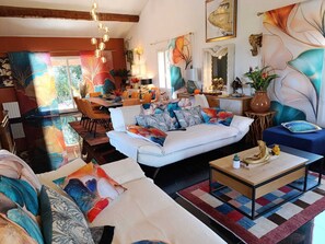 A spacious living room with a white sofa, colorful cushions, a coffee table, and a dining area with chairs.