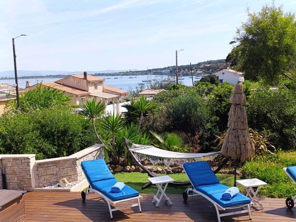 A deck with lounge chairs, a hammock, and a view of a marina with boats.