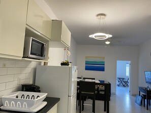 Eine moderne Küche mit weißen Schränken, einer Mikrowelle und einem Kühlschrank. Es gibt eine Essecke mit Tisch und Stühlen, sowie ein Gemälde an der Wand.