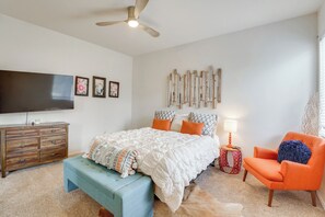 Quarto com cama, cômoda, televisão, cadeira e uma obra de arte na parede.