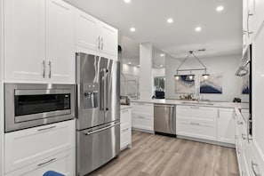 A modern kitchen with stainless steel appliances, white cabinetry, and a wooden floor.