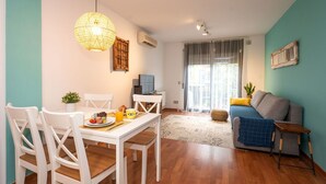 A modern living room with a dining area, wooden flooring, a blue sofa, and a hanging light fixture.