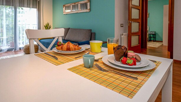 A dining area with a table set for breakfast, including croissants, strawberries, and a cup of orange juice.