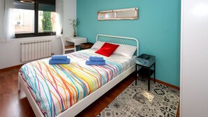 A bedroom with a bed, a desk, a chair, a radiator, and a window with curtains.