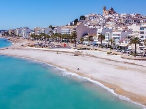 Perched atop a hill, a historic church stands proudly alongside the town's picturesque beach, surrounded by palm trees and white buildings.