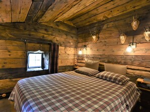 Quarto rústico de cabana com colcha xadrez, paredes de madeira, janela com cortinas e caveiras de animais montadas na parede.