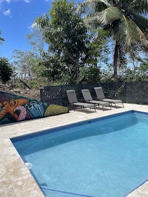 Una piscina con borde de azulejos, sillas de descanso y un mural en la pared.