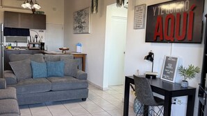 A modern living room with a grey sofa, a dining table with chairs, and a kitchen in the background. - Ocean View Home with private pool and parking. Sleeps 13 (Rincon)