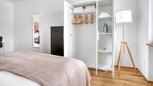 Une chambre à coucher avec un lit, une armoire, un miroir et une lampe sur pied.