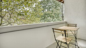 Un balcon avec une table et des chaises, une vue sur les arbres et un mur blanc.
