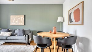 Un salon moderne avec un canapé gris, une table ronde en bois entourée de chaises et un vase posé sur la table.