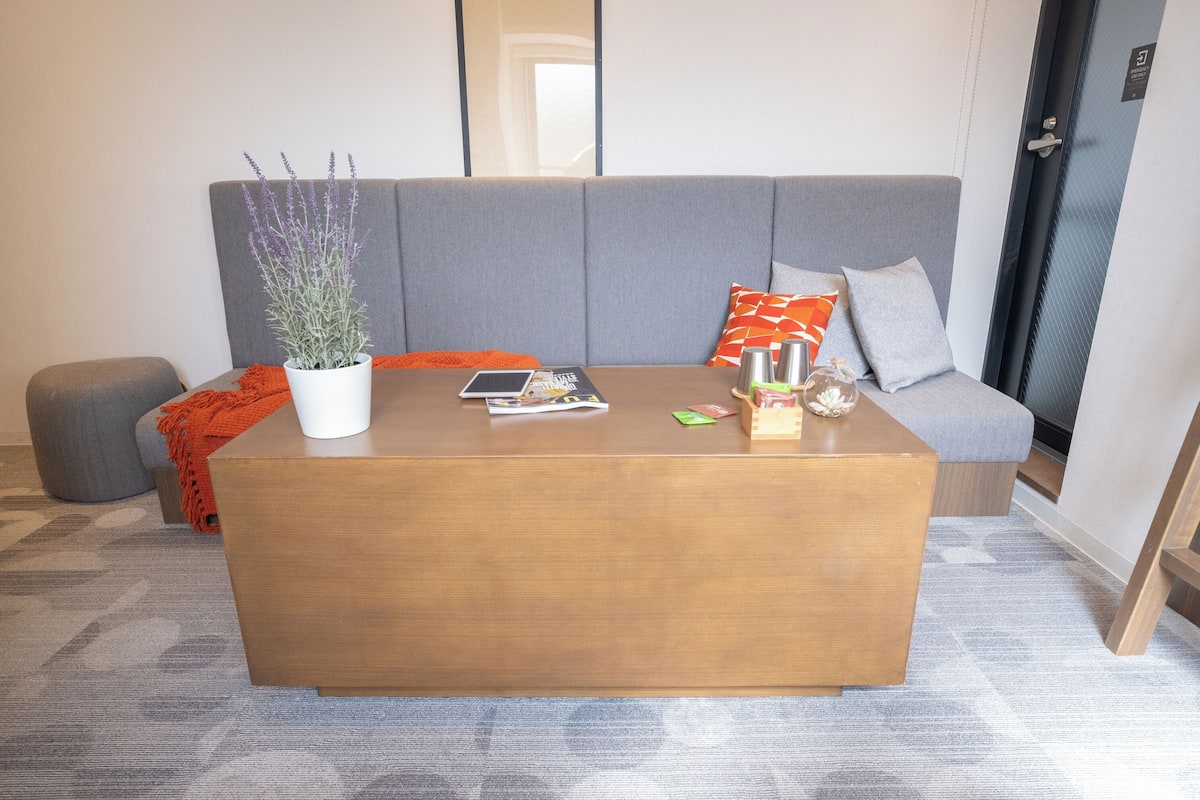 A modern living room with a grey sofa, a wooden coffee table, a potted plant, and a red throw blanket.