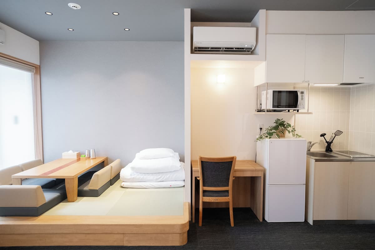 A compact hotel room with a bed, a small desk, a chair, a microwave, and a refrigerator.