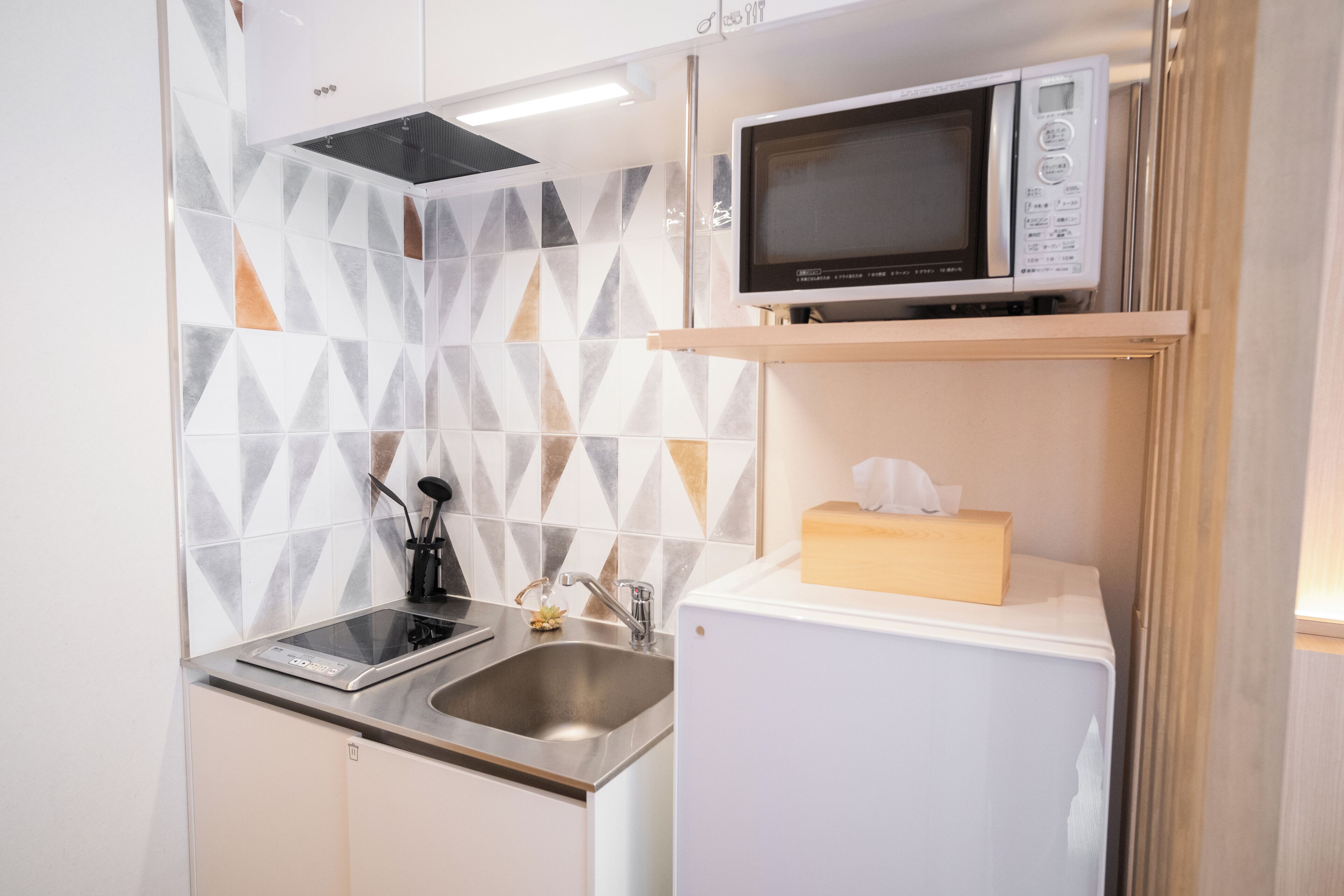 A compact kitchen with a microwave on a shelf, a sink, and a small refrigerator.
