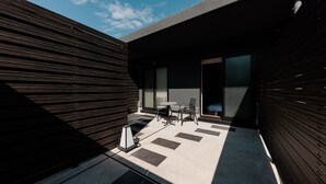 A modern outdoor patio with a dining table and chairs, a small garden area, and a view of the sky. - ORI Rokkaku (Kyoto)