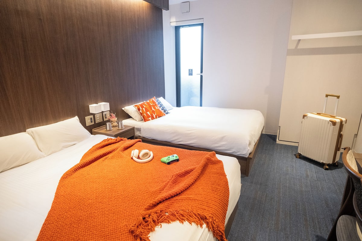 A hotel room with two beds, a wooden headboard, a radiator, and a suitcase.