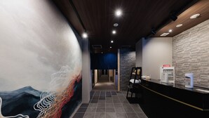 A hotel reception area with a modern design, featuring a black reception desk, a wall-mounted information kiosk, and a mural with abstract patterns. - ORI Rokkaku (Kyoto)