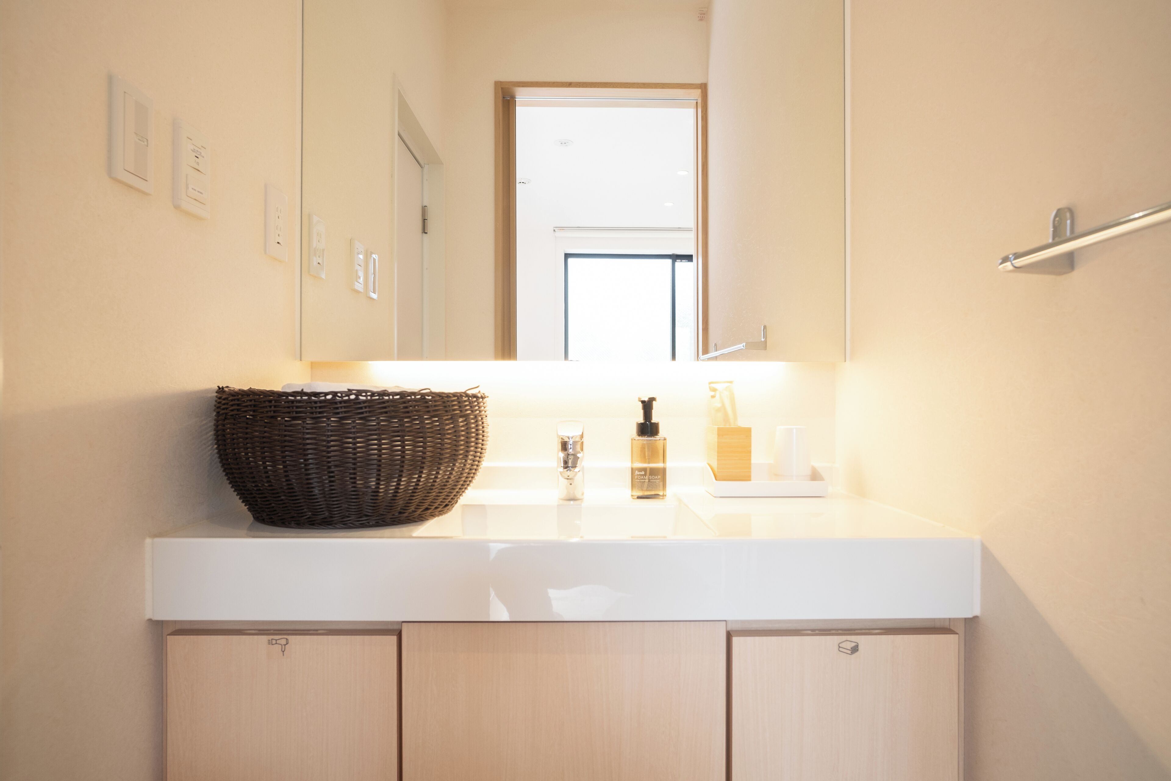 A bathroom with a white countertop, a wicker basket, a bottle, and a mirror.